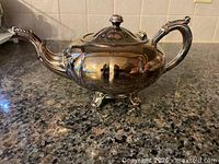 Side view of silver-plated teapot showing feet, handle and spout