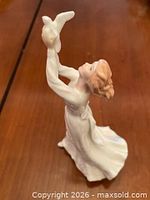 Angled side view of figurine showing raised arms, dove, gown detail