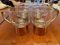 Front view of six clear glass espresso cups showing stainless steel bases and handles