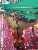 Violin standing outside hard case with bow and rosin visible
