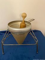 Side view of aluminum strainer seated in wire stand with wood pestle