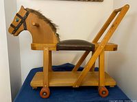 Right side view of wooden ride-on horse showing seat, handle and wheels