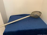 Full view of long metal scoop on blue surface