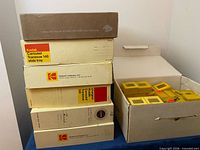 Stacked Kodak Carousel Transvue 140 slide tray boxes and grey case beside cardboard box of yellow Kodachrome slide boxes