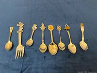 Front view of eight souvenir flatware pieces laid out on blue surface