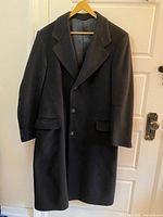 Full view of black three-button overcoat on hanger