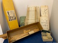 Yellow Model Shipways box standing with contents displayed: wood pieces, plans, fittings boxes