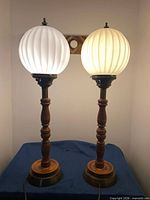 Front view of both lit table lamps showing wood bases and milk glass globes