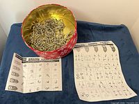 Open red tin with numerous metal puzzles and two instruction sheets