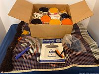 Open box with wool rolls, hooks, booklet, and canvas displayed