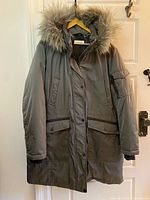Front view of grey Calvin Klein parka on hanger showing hood with faux fur, flap pockets, full length