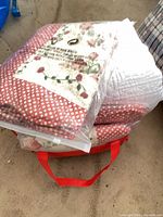 Stack of four sealed floral patchwork quilts inside clear bags with red fabric tote visible