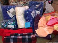 Sealed blue packages, rolled cream fleece, red plaid fleece, floral swimsuit package and assorted pastel towels