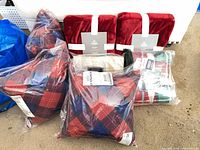 Front view showing two red velvet throws with paper bands, three plaid pillows, beige plaid throw and chevron throw in plastic