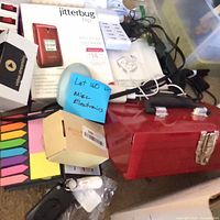 Group view showing Jitterbug phone box, red toolbox, cables, sticky notes, keychain remote