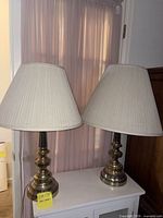 Pair of brass table lamps with shades on cabinet