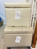 Two stacked white faux leather ottomans, larger on wheels, smaller on top