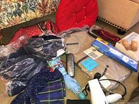 Group view of clothing in packaging, scarves, pillow, eyeglass case, hair dryer and accessories on floor