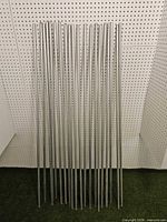 Twenty steel conduit pieces leaned against pegboard wall