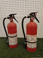 Front view of both fire extinguishers showing height, hoses, and labels