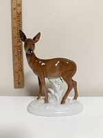 Front view of brown porcelain doe on white base with ruler for scale