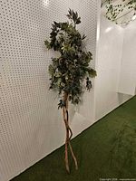 Full view of tall artificial tree standing on intertwined trunk without planter