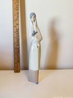 Front view of porcelain figurine showing woman holding grey rabbit next to ruler for scale