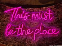 Full view of illuminated pink LED sign reading “This must be the place”