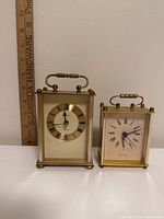 Front view of both brass carriage clocks with ruler for scale