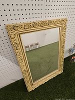 Front view of cream ornate framed mirror leaning against pegboard wall