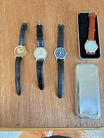 Four wristwatches laid out with storage tin