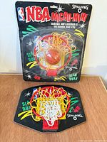 Packaged Spalding NBA Micro-Mini hoop set displayed above loose matching hoop set on wood surface