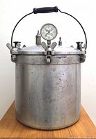 Front view of aluminum pressure canner showing cylinder body, bail handle, pressure gauge, clamps