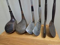 Front view of six vintage golf club heads showing wood and metal construction