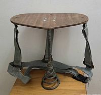 Front view of milking stool showing wood seat, metal leg, coil spring and straps
