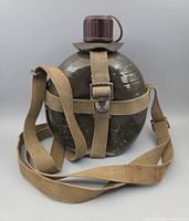 Front view of olive drab canteen with attached tan canvas strap and brown cap