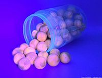 Jar tipped with 20 yellow glass marbles glowing under ultraviolet light