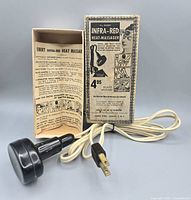 Massager with cord beside open box displaying folded instructions