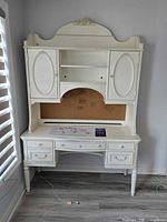 Front view of white desk with attached hutch showing drawers, doors, shelves, cork board, power cord