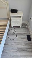 Full view of white nightstand beside bed frame, showing drawer opening, cabinet door, and bun feet