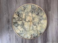 front view of round marble-look wall clock with gold bezel and markers