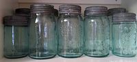 Front view of seven aqua Crown canning jars with lids