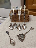 Seven spoons upright in woven basket with three additional spoons laid in front, showing overall lot