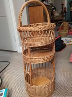 Full view of round three-tier wicker and wood shelf showing handle, tiers, and overall condition