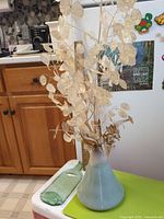 Vase with dried stems beside green fused glass bottle on surface