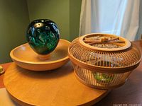Green glass paperweight on footed wood bowl beside bamboo basket on wood platter