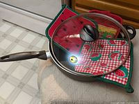 Frying pan with glass lid resting on three pot holders