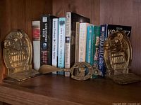 Front view of both horse bookends, shoehorn laid between, seven books standing behind