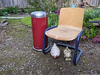 Red metal trash can, plywood chair, ceramic chicken and cat on ground