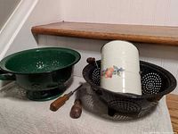 Green colander, black colander, Bromwell's cream sifter, two wood-handled screwdrivers on surface
